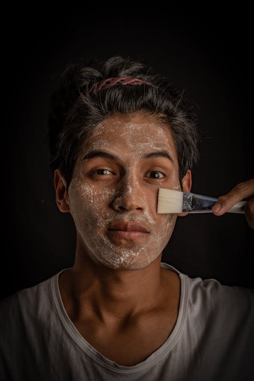 Young Man Spreading a White Face Mask with a Brush on His Face 