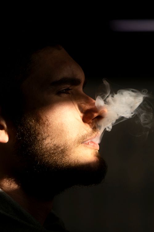 Free Artistic close-up of a young man exhaling smoke in dramatic lighting. Stock Photo