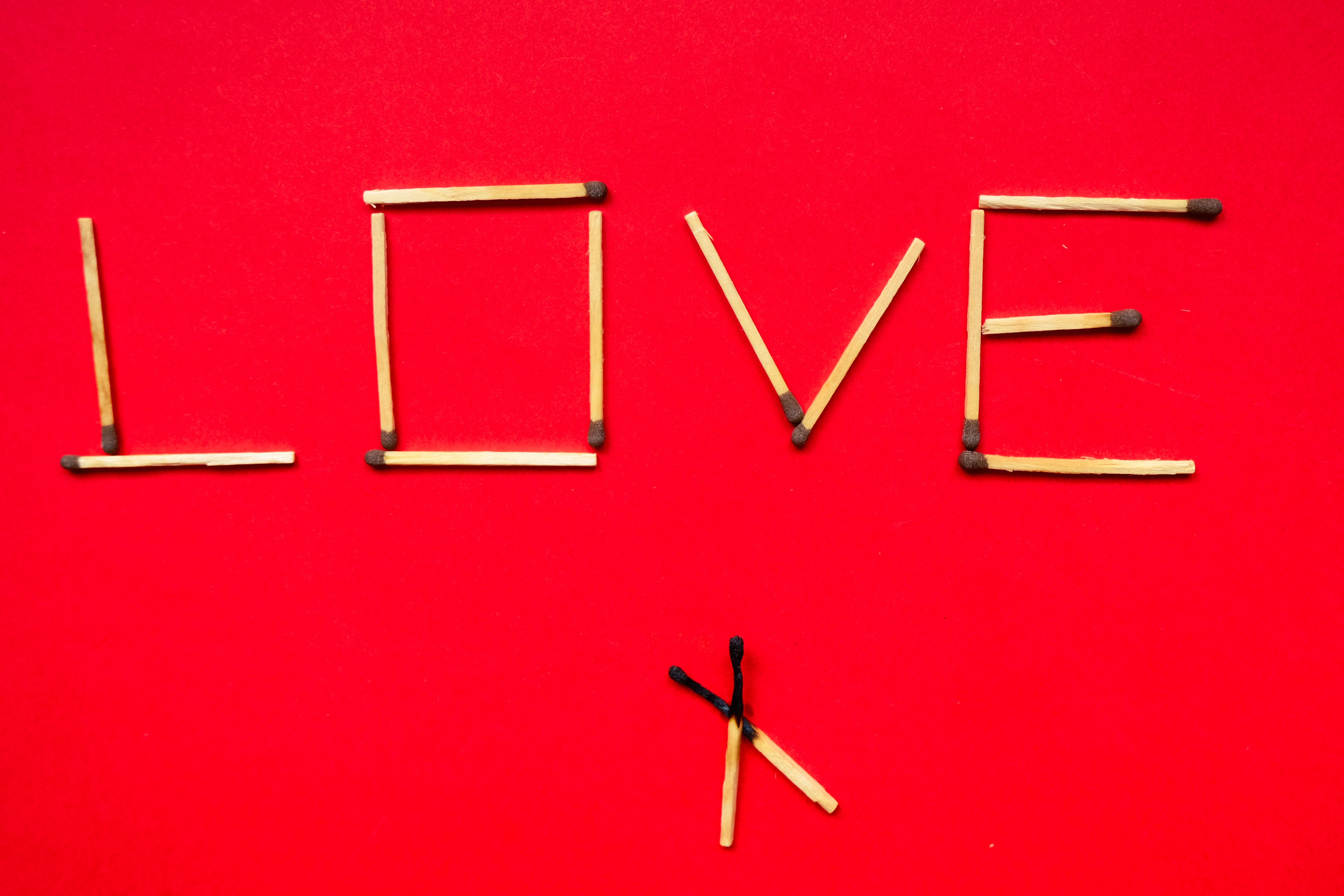 Creative arrangement of matchsticks spelling love on a vibrant red background.