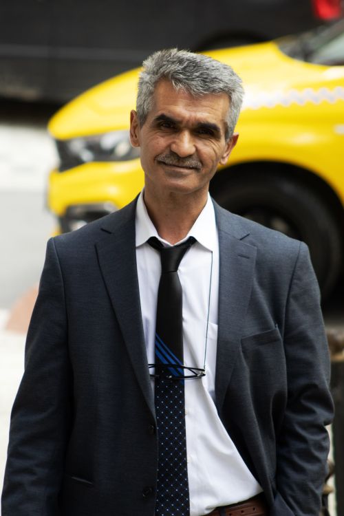 Free Confident middle-aged businessman in a suit, smiling outdoors with a yellow taxi in the background. Stock Photo