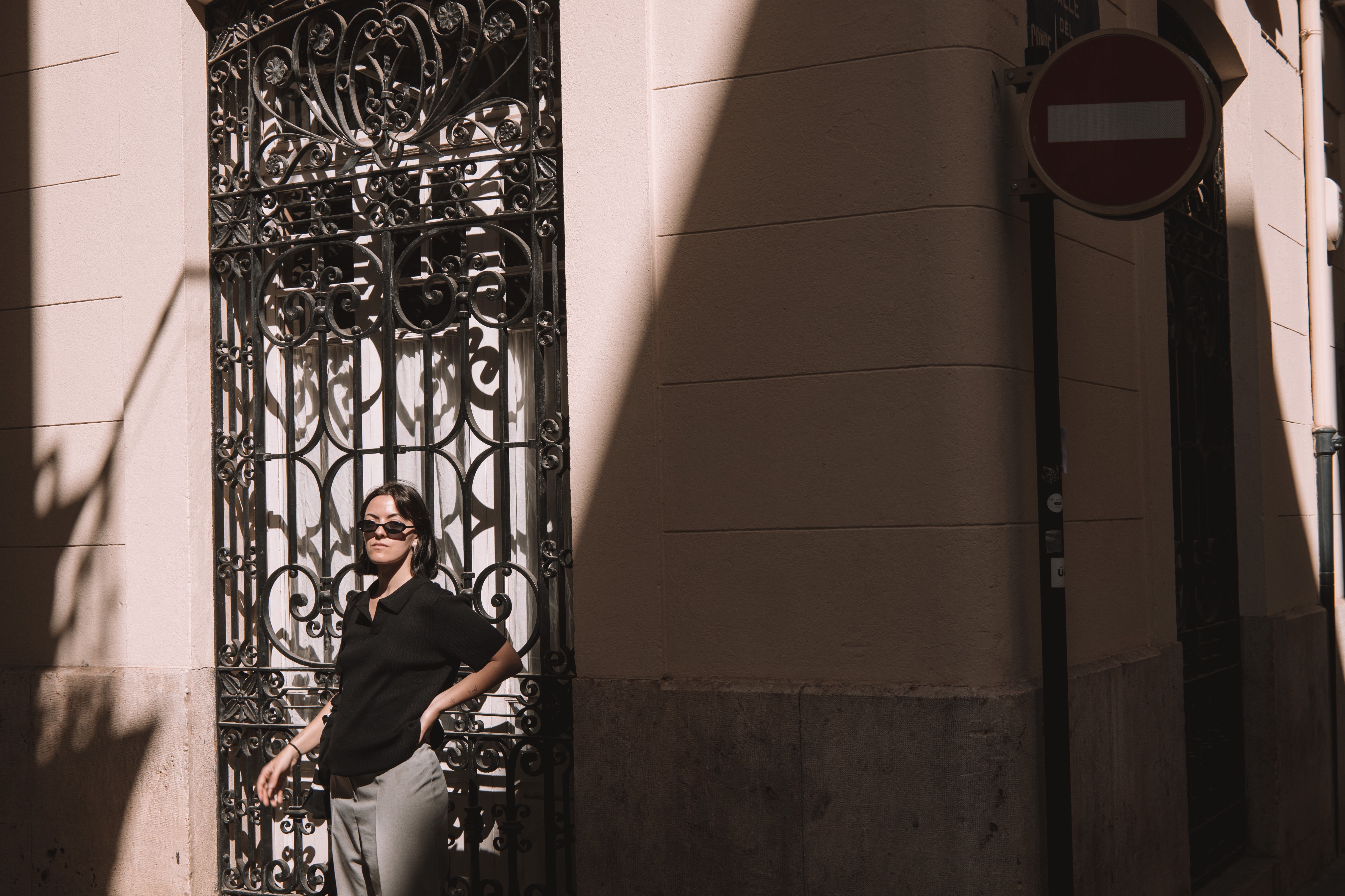 Fashionable woman in black polo posing with sunglasses on a sunny street in Valencia, Spain