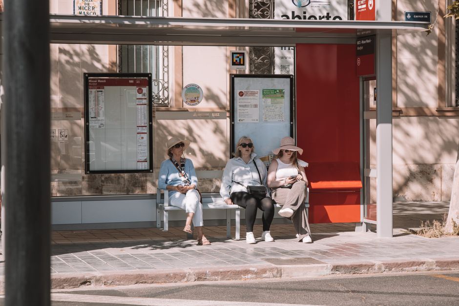 Tres mujeres sentadas en una parada de autobús en la soleada Valencia, España, mostrando la vida urbana.