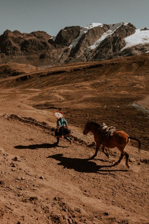 Free A person in traditional attire riding a horse along a sunlit mountain path. Stock Photo