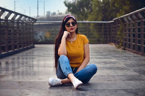 Free A fashionable young woman in casual attire sitting on an urban walkway outdoors. Stock Photo