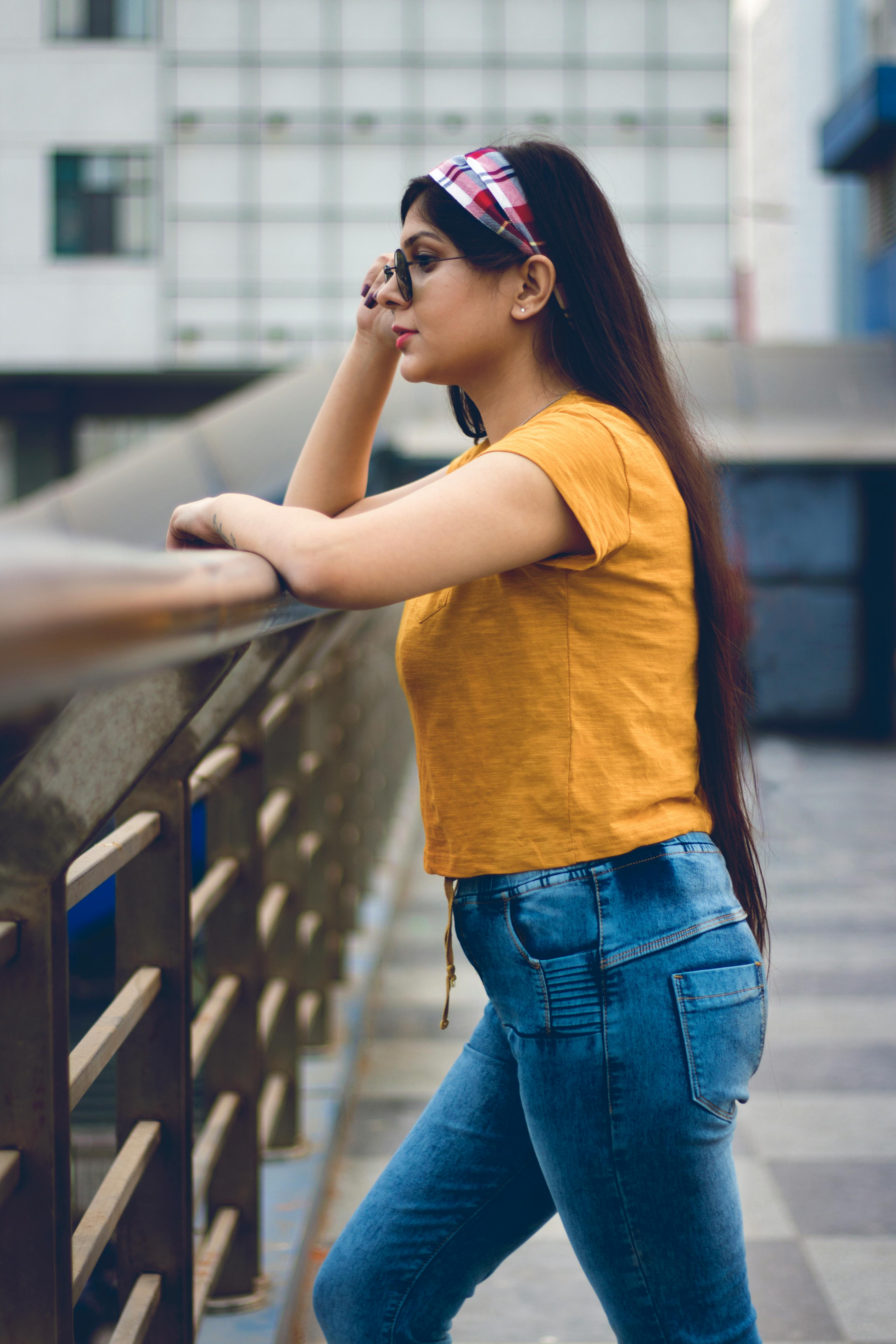 一位穿着黄色上衣和牛仔裤的时尚年轻女子在现代城市环境中户外摆姿势