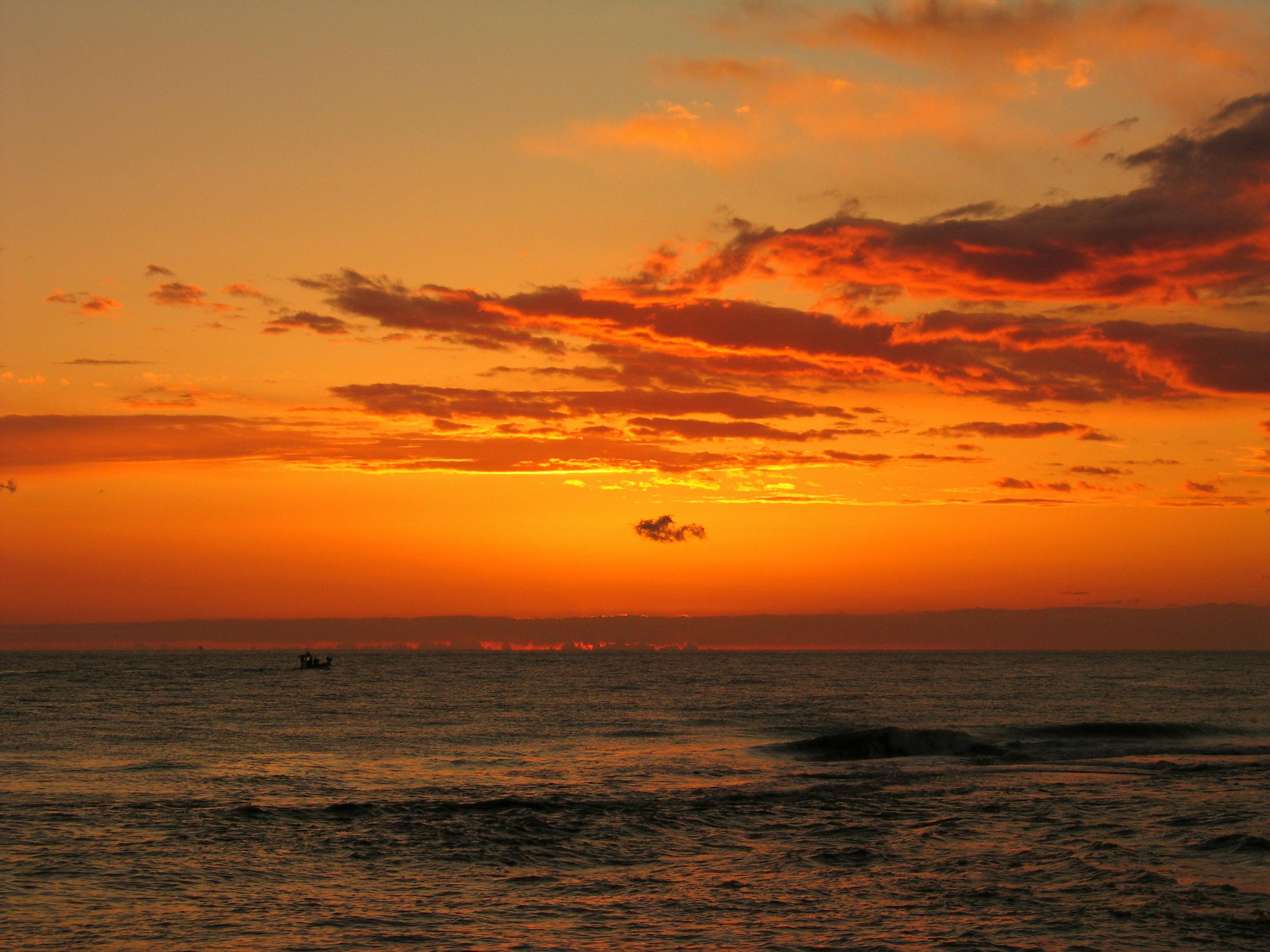 a sunset over the ocean with a boat in the water