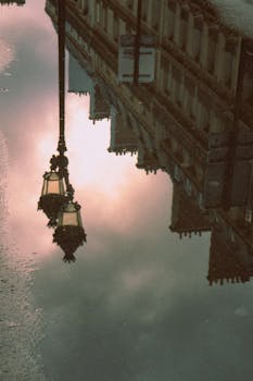 Artistic reflection of Parisian street lamps and architecture in a puddle at dawn creating a moody ambiance.