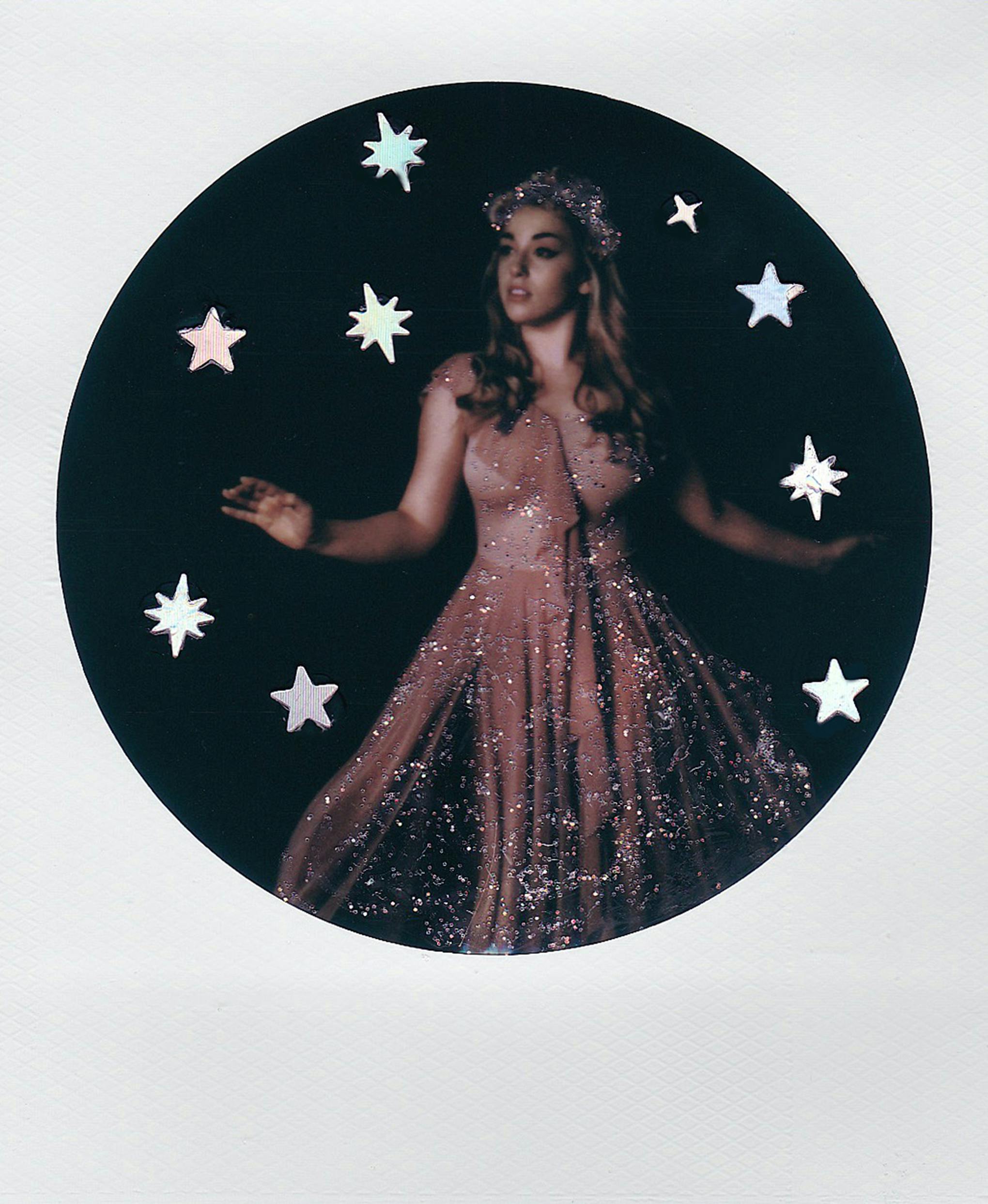 A woman poses in a sparkling dress surrounded by stars, giving an ethereal feel.