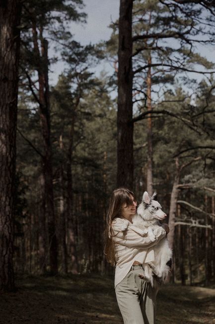 Young woman holding a fluffy dog in a peaceful forest, showcasing companionship and nature's tranquility.