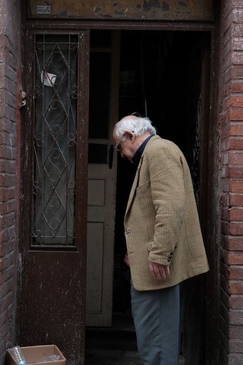Free An elderly man in a jacket stands at a rustic doorway framed by brick walls. Stock Photo