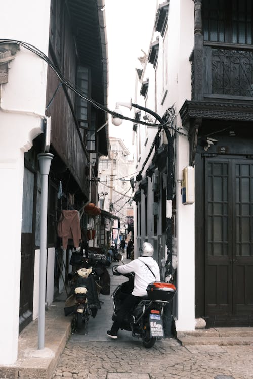 Man Riding a Motorcycle in a Narrow City Street 