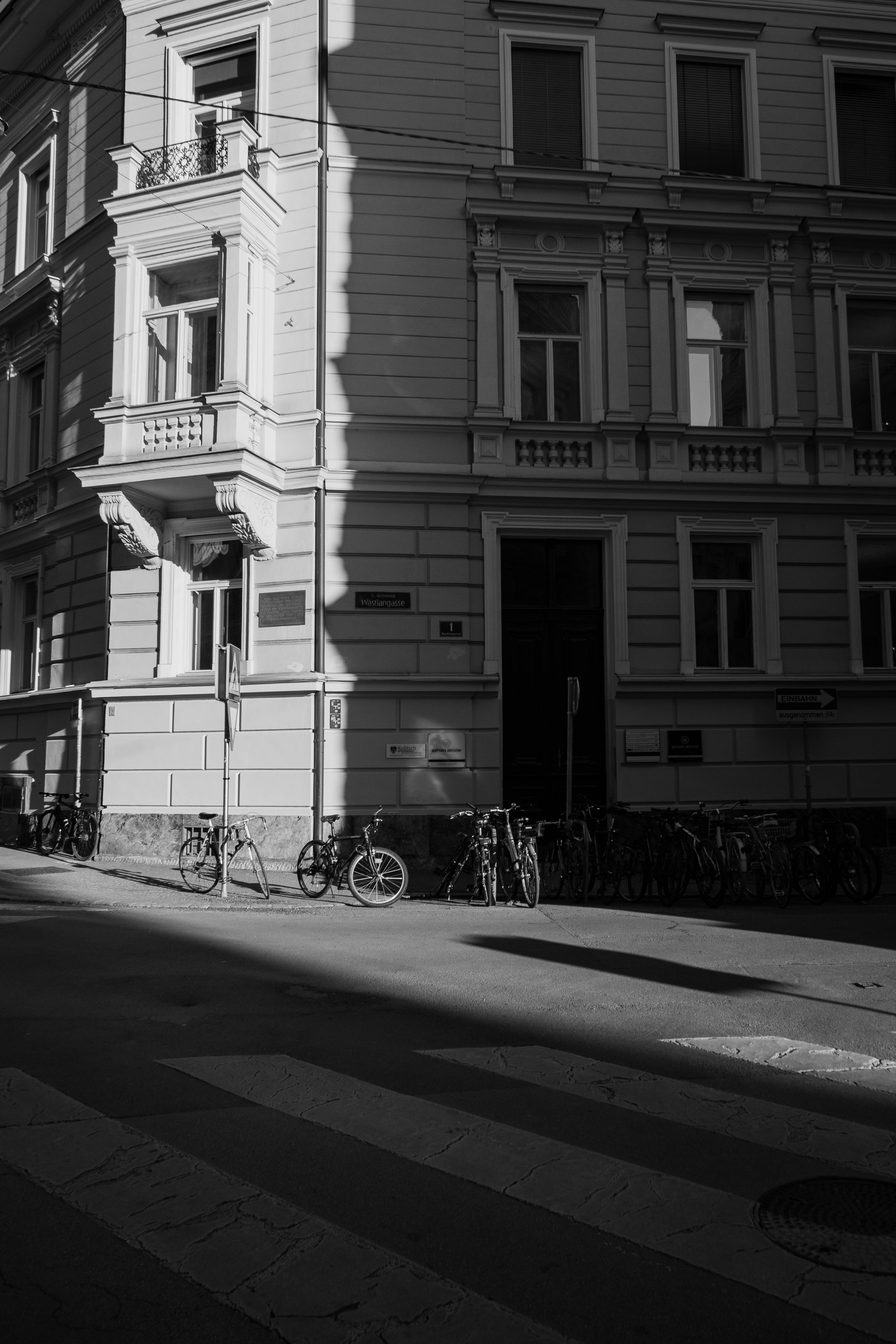 Grayscale view of a residential street corner in Graz, Austria, with bicycles lining the building facade.
