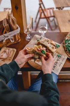 Person holding a delicious sandwich at a rustic cafe table, perfect for lunch or a hearty brunch.