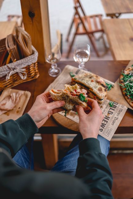 Person holding a delicious sandwich at a rustic cafe table, perfect for lunch or a hearty brunch.