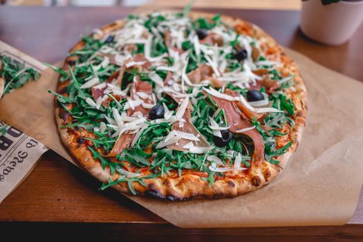 Mouthwatering homemade pizza topped with fresh arugula, prosciutto, and olives on a crispy crust.