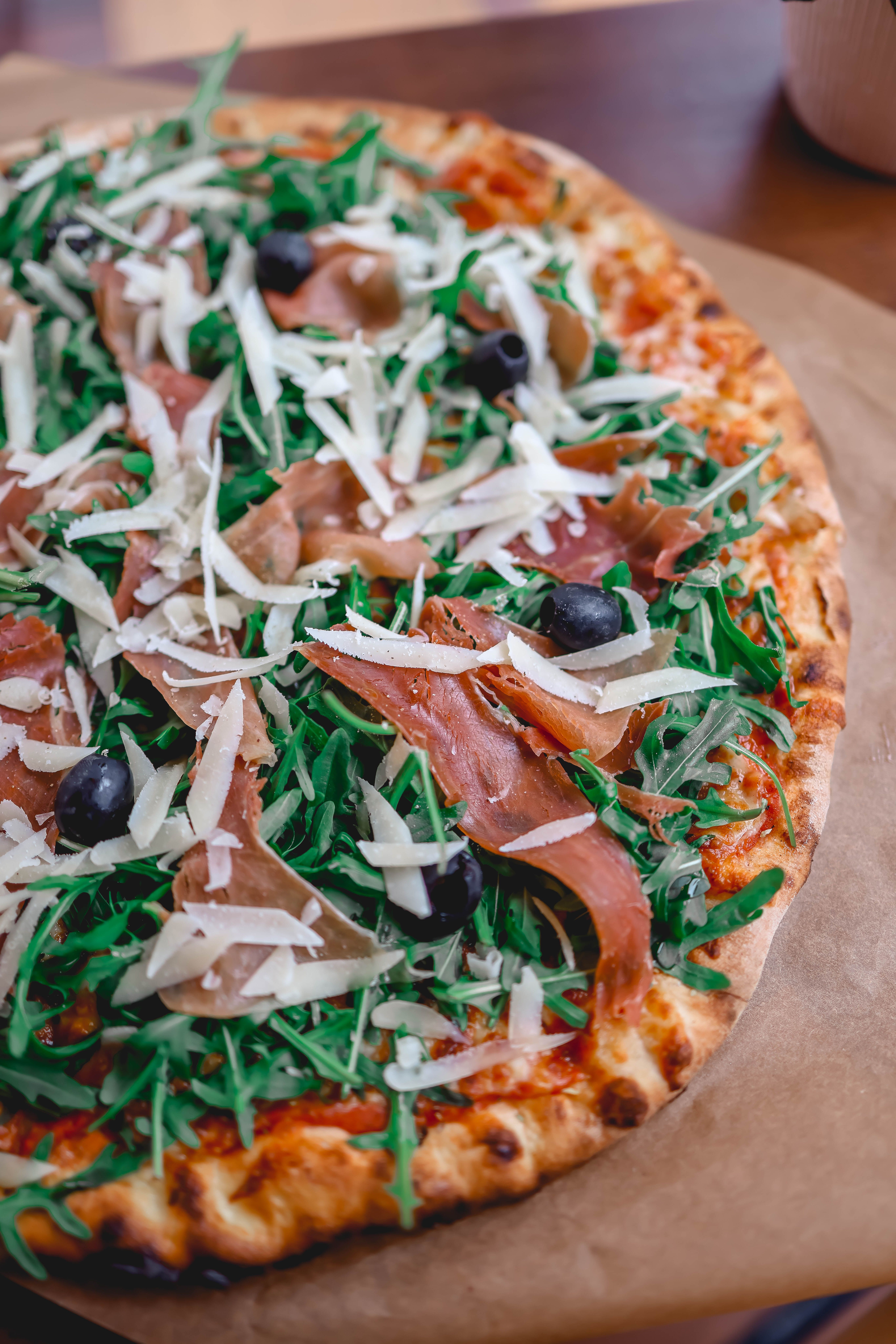 Tasty pizza topped with arugula, prosciutto, olives, and cheese, perfect for lunch or dinner.