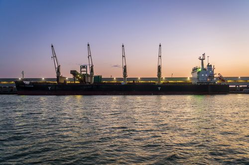 Free A docked bulk carrier ship with cranes at sunset, reflecting in the harbor water. Stock Photo