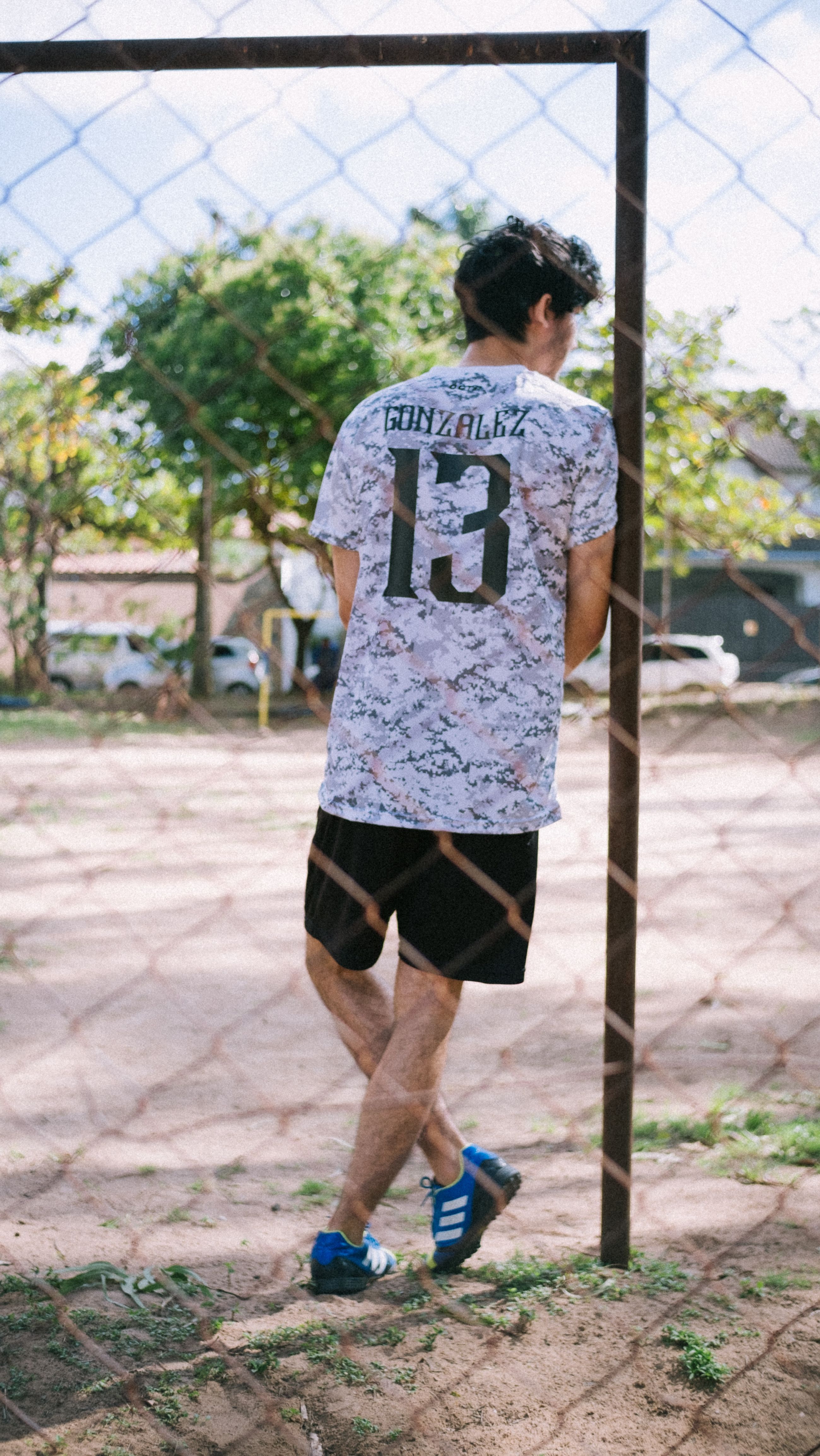 A young man wearing a sports jersey standing by an outdoor soccer goal on a sunny day.