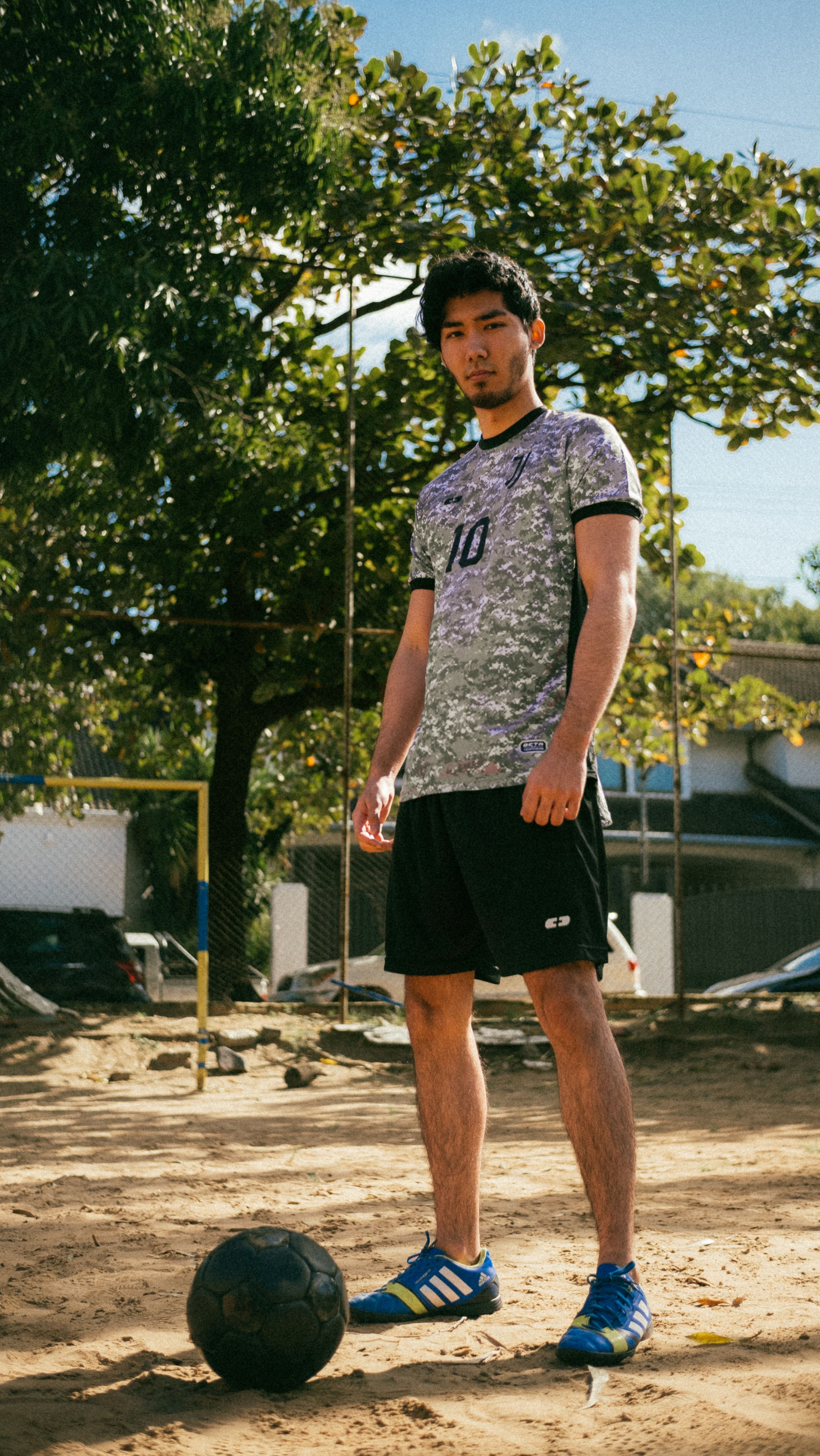 Young man enjoying a game of football on a sunny day in a sandy outdoor pitch.