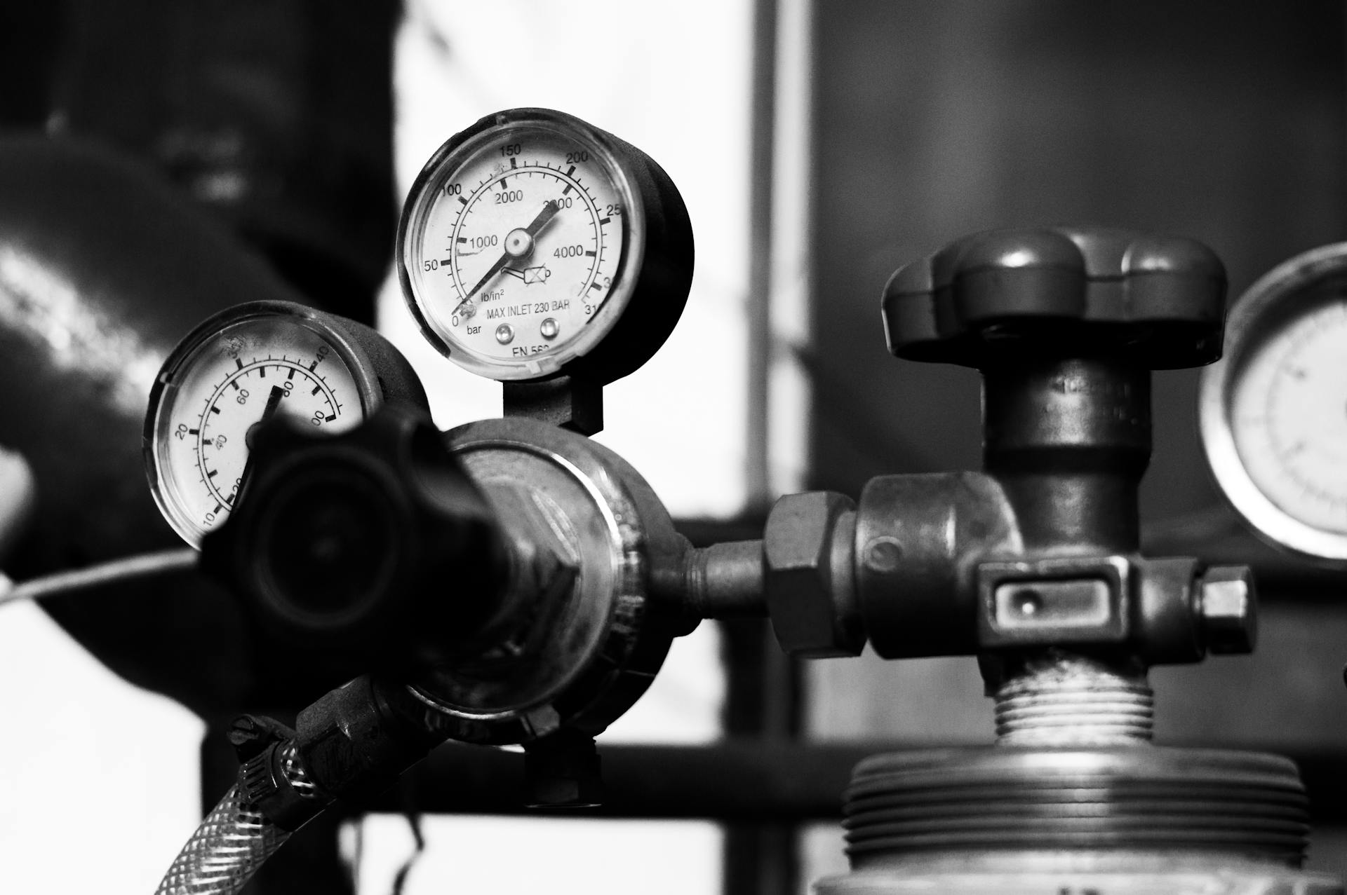 Black and white close-up of vintage pressure gauges and industrial metal machinery.