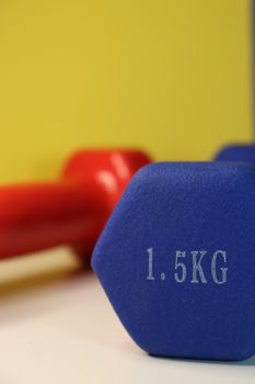 Close-up of blue and red dumbbells on a yellow background, emphasizing fitness and sport.