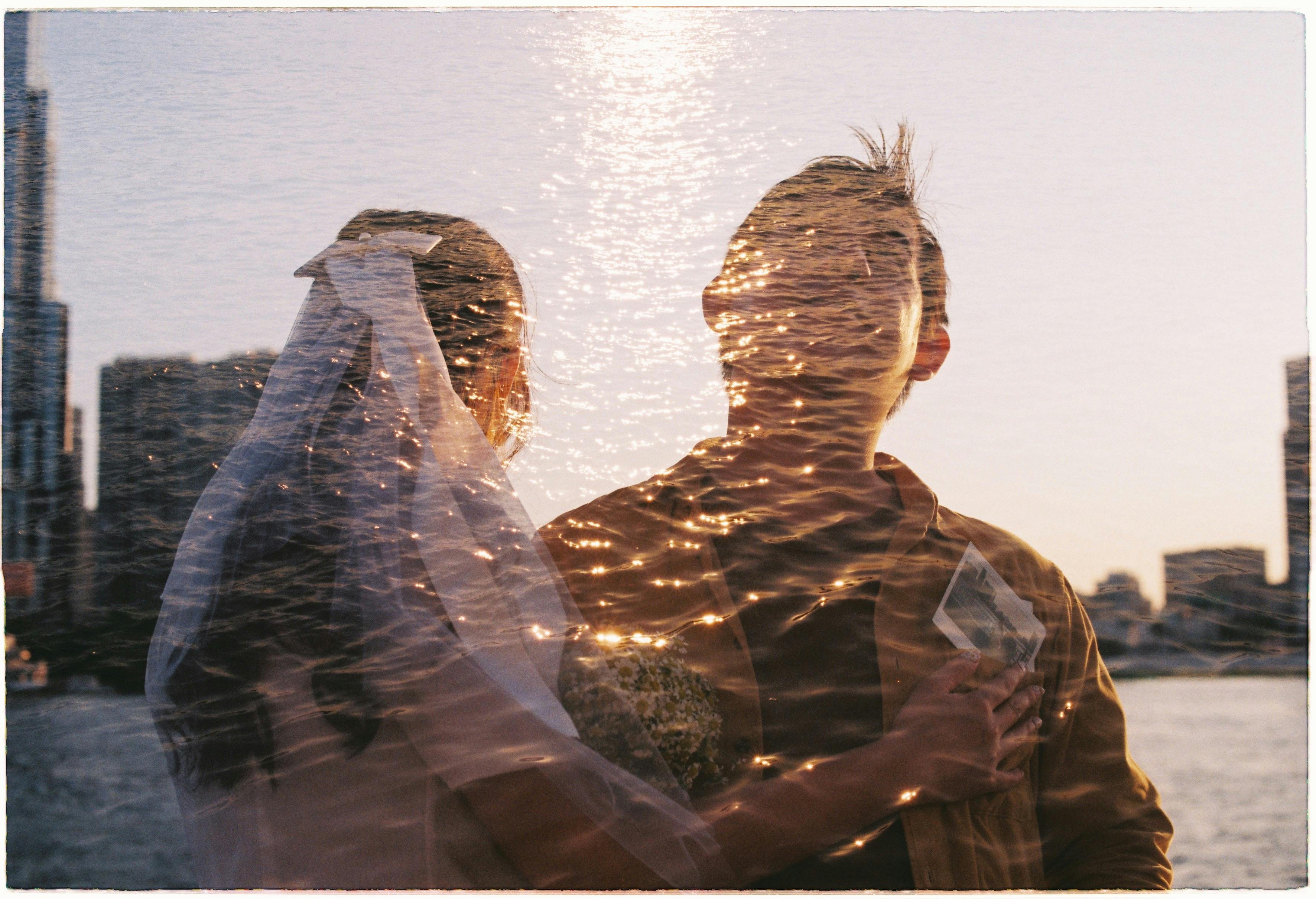 A creative double exposure photo of a couple on their wedding day against a city skyline and water reflection.
