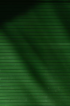Abstract green metal wall with horizontal lines and shadow patterns creating texture.