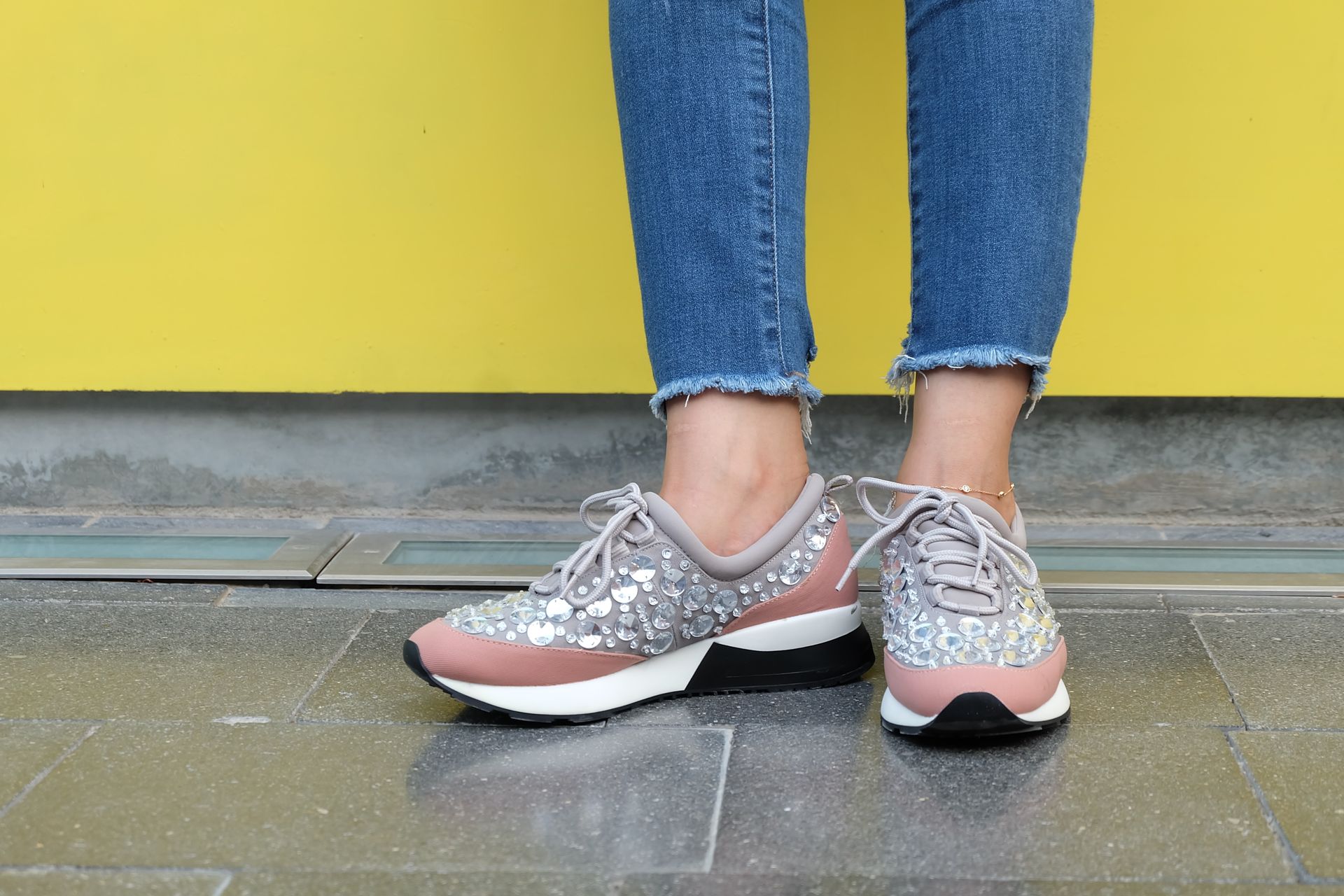 Close-up of stylish sneakers with sequins paired with blue denim against a yellow background.