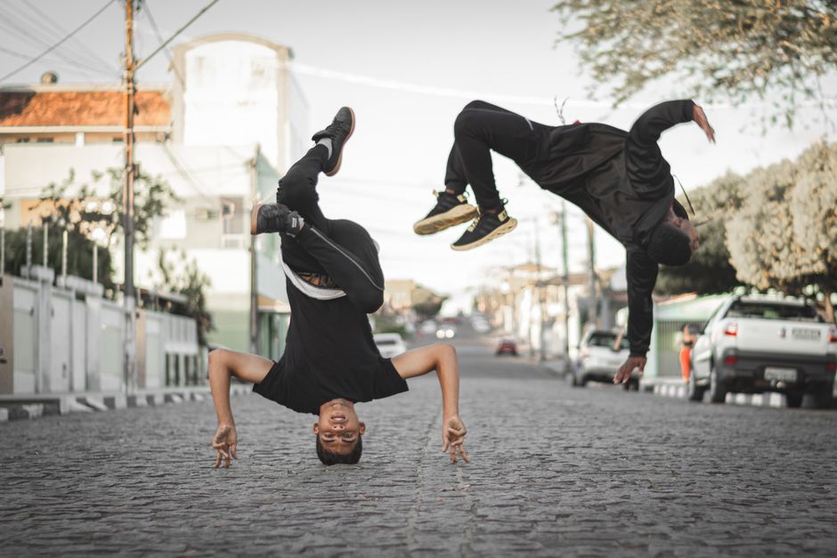 Two men performing breakdancing moves on a cobblestone city street outdoors.