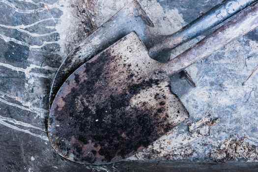 A detailed close-up of worn, rusty shovels lying on a concrete surface, highlighting textures.