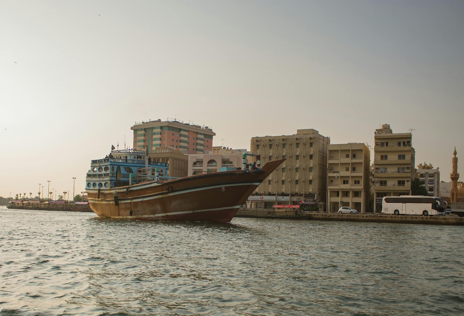 Scenic view of a traditional Arabic dhow sailing on Dubai Creek with urban skyline backdrop.