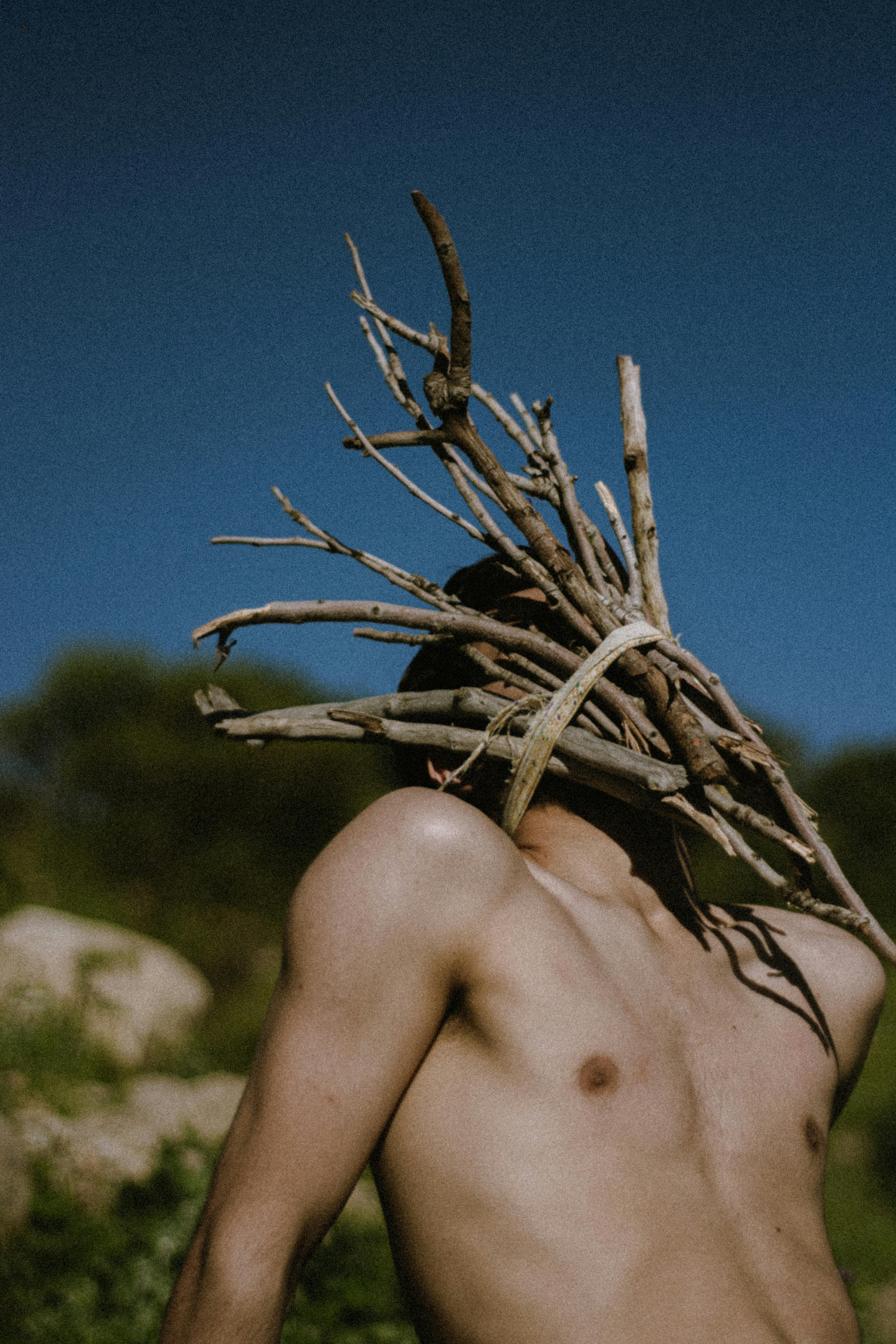 Shirtless man carrying firewood outdoors in Erbil, Iraq.