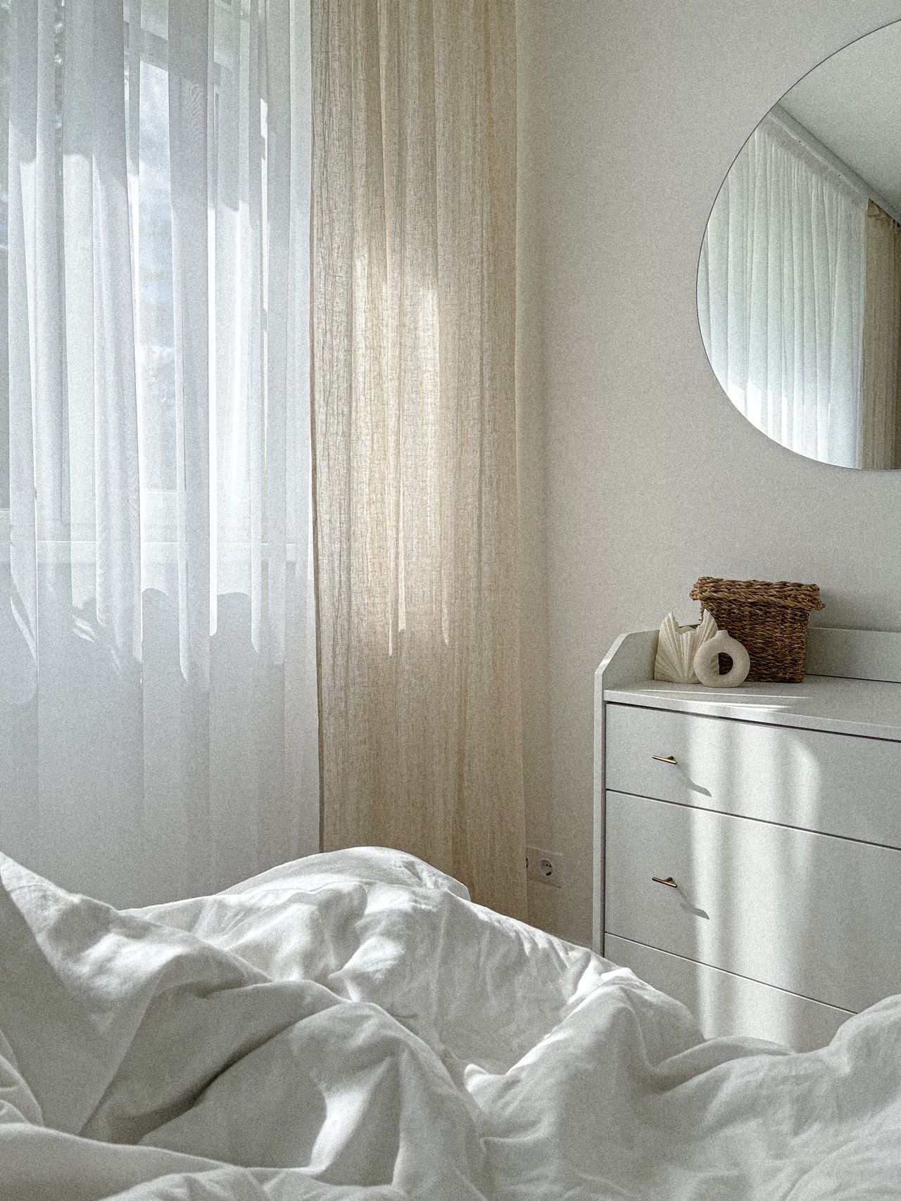 White dresser with dark hardware and a round mirror in a bright bedroom corner