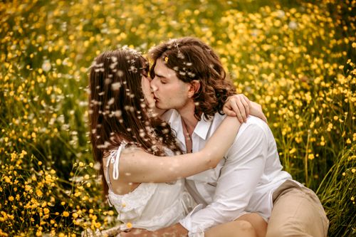 Free A couple embraces and kisses amidst vibrant yellow wildflowers in a sunny meadow. Stock Photo