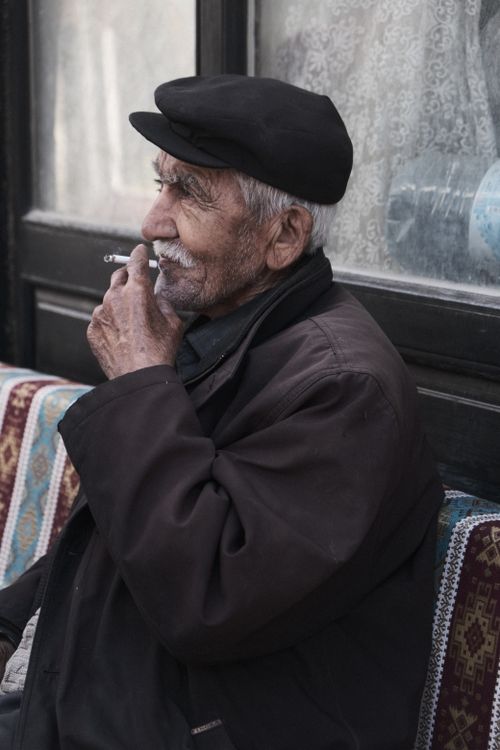 Free Elderly man wearing a hat, sitting outdoors and smoking with a thoughtful expression. Stock Photo