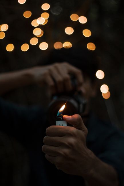 Person holding a lighter with bokeh lights in the background, creating a creative and moody effect.