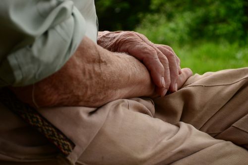 Free Close-up of senior's hands resting peacefully on a lap outdoors, symbolizing quiet contemplation. Stock Photo