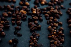 A close-up of roasted coffee beans scattered on a dark surface, highlighting their rich texture and color.