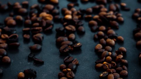 A close-up of roasted coffee beans scattered on a dark surface, highlighting their rich texture and color.