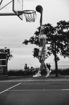 A thrilling moment of a man dunking a basketball outdoors, captured in black and white.