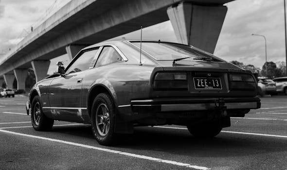 Black and white photo of a vintage sports car on city streets under an overpass.