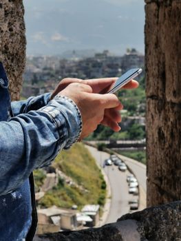 A person using a smartphone from a high vantage point overlooking a scenic city road.