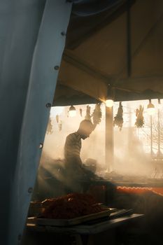 Silhouette of a vendor in a bustling evening market stall with glowing sunset.