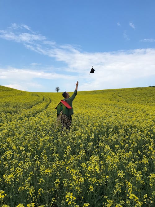 Man Tossing His Hat in the Air on a Field with Rapeseed Flowers