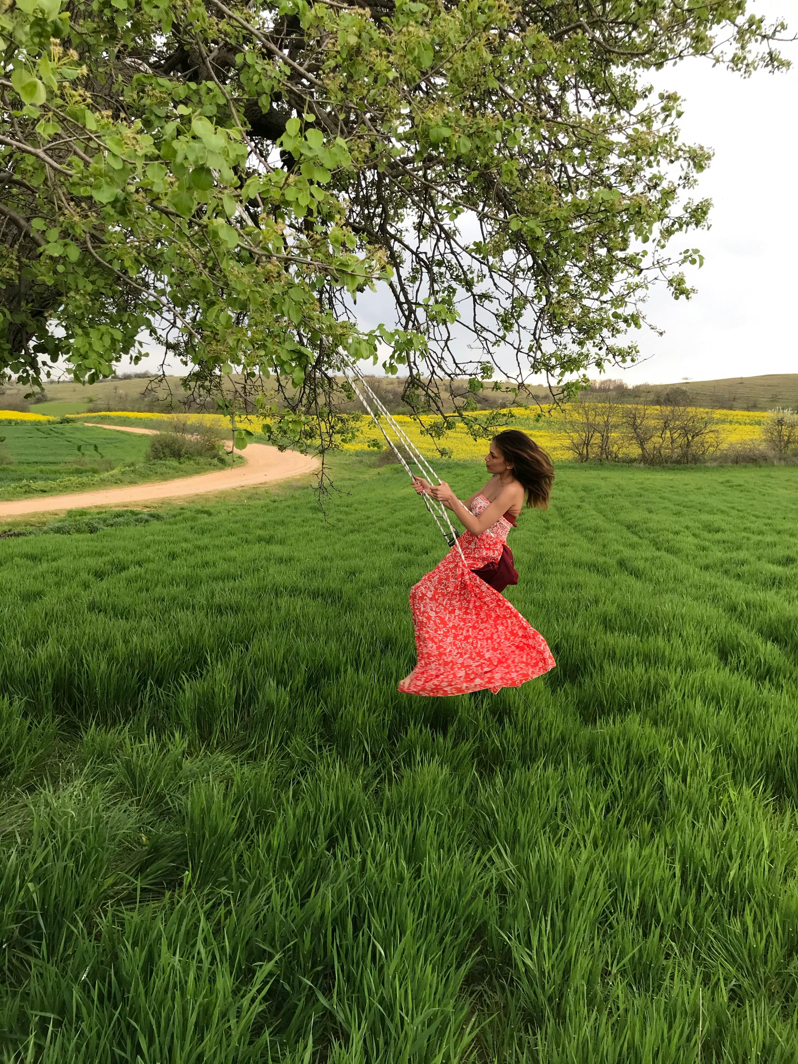 A carefree woman enjoys swinging on a tree swing in a lush green meadow during springtime.