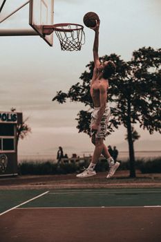Young man executing a high jump dunk on an outdoor basketball court, showcasing athleticism.