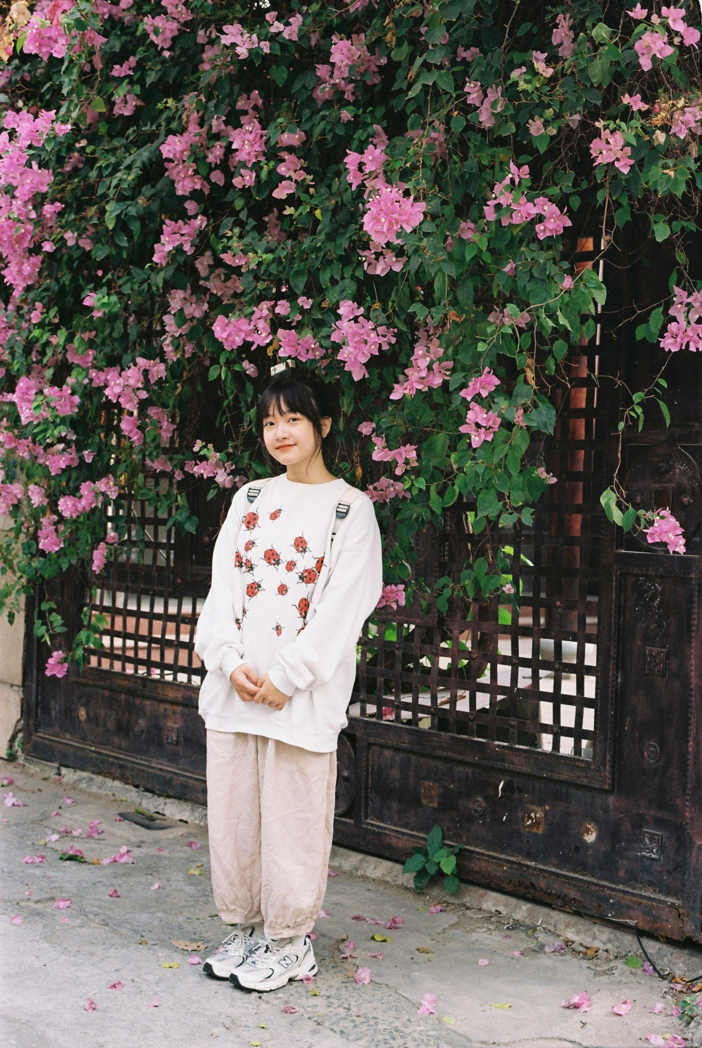 Casual outfit of a young woman standing beside vibrant pink flowers on a sunny day.