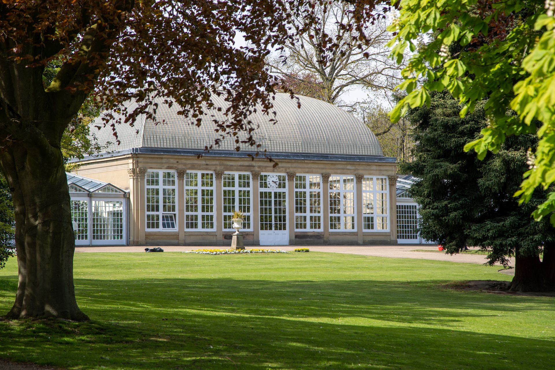 A beautifully clear view of a botanical garden dome surrounded by lush green trees and grass.