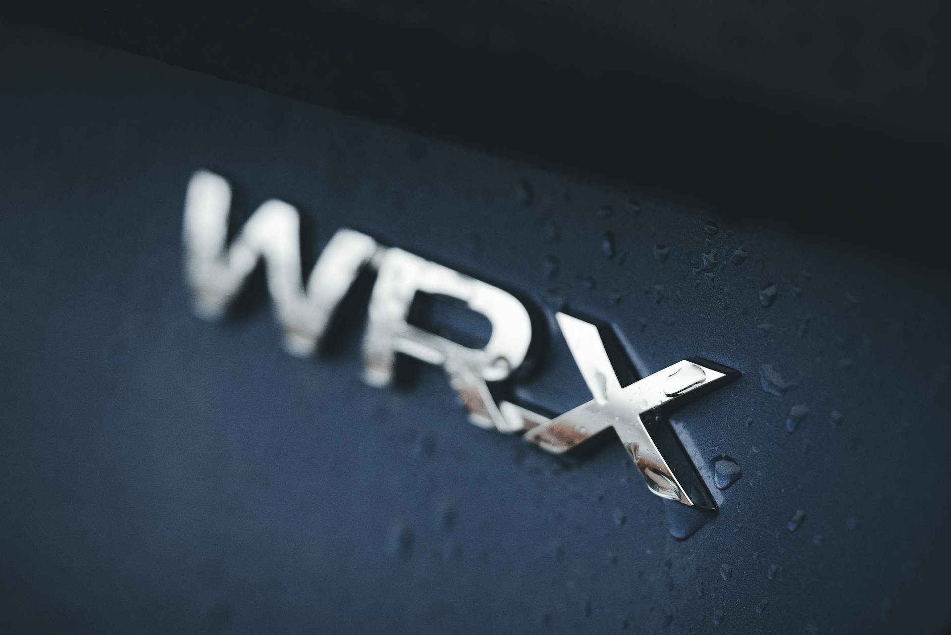 Detailed view of Subaru Impreza WRX badge with water droplets on surface, emphasizing elegance.