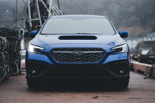 Free Front view of a blue sports car, likely a Subaru, on wet pavement in an overcast outdoor setting. Stock Photo